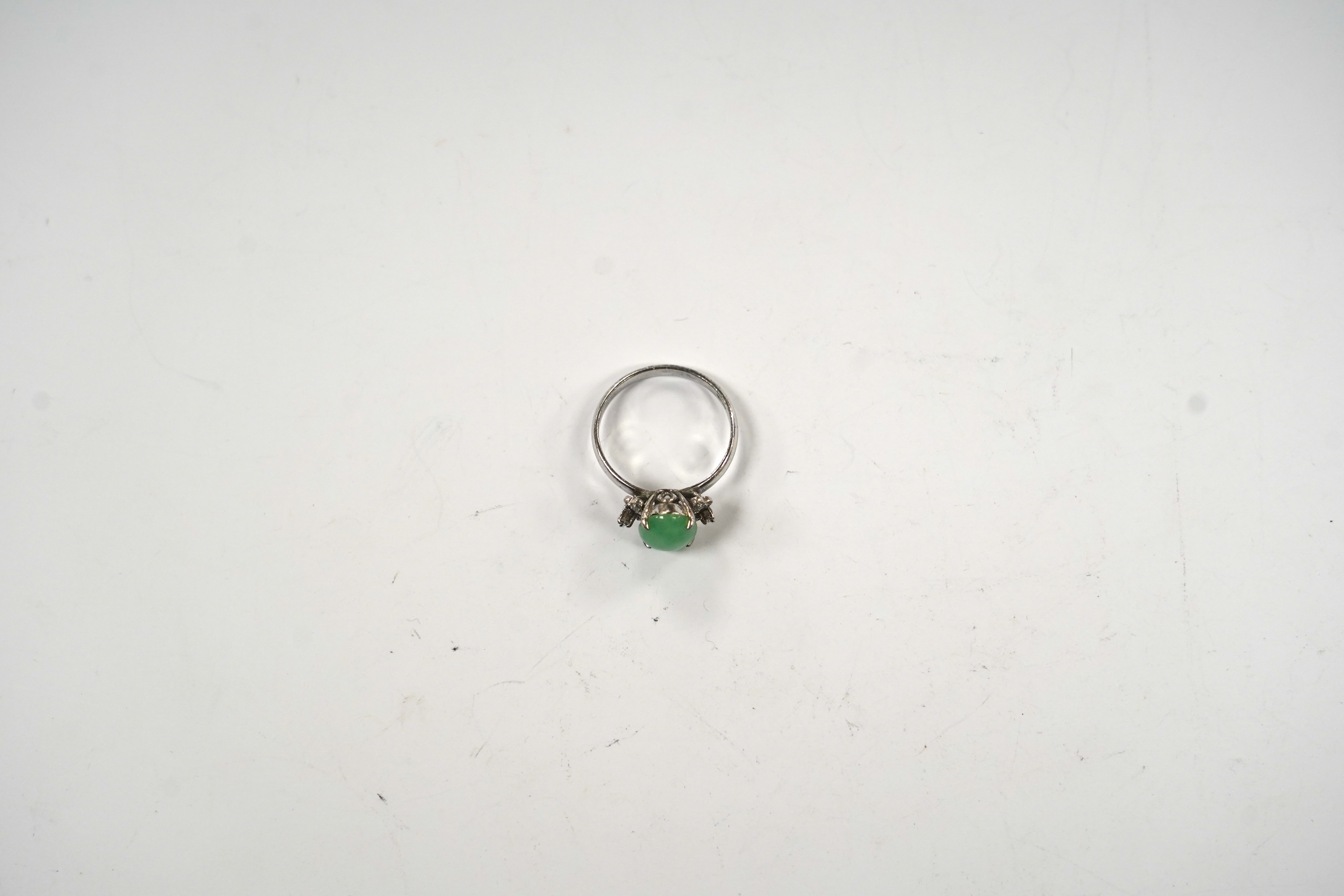 A modern 18k white metal and single stone cabochon jade and six stone diamond chip set ring, size O, gross weight 3 grams.